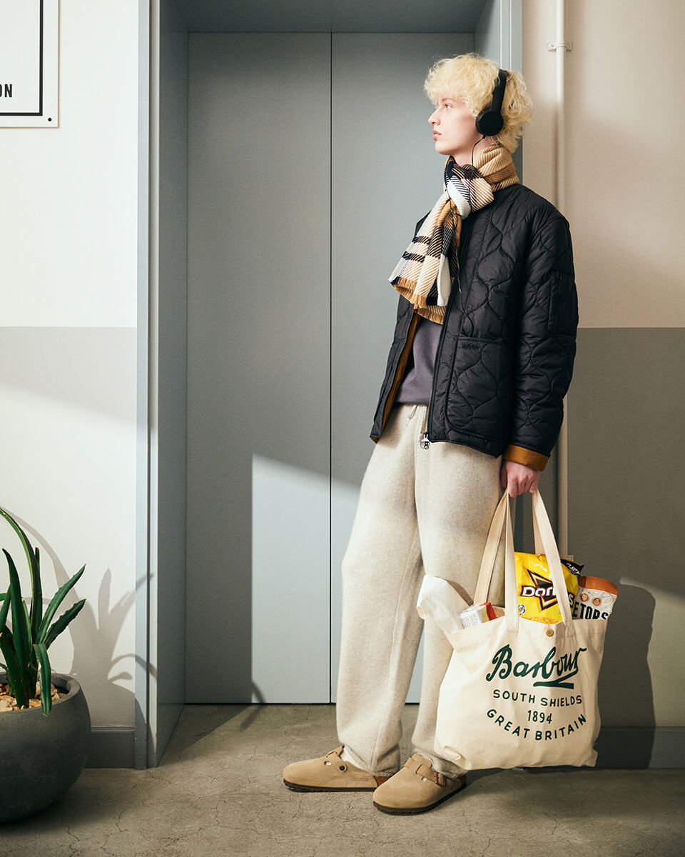 ブラックのジャケット・ベージュのトートバッグを着用した男性